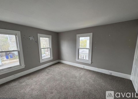 A room with grey walls and carpeted floor with two windows.