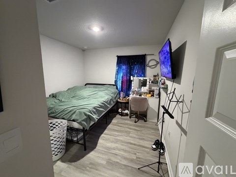 A bedroom with a bed, desk, chair, and a television mounted on the wall.
