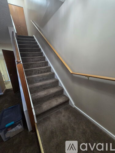 A staircase with a wooden handrail and carpeted steps.