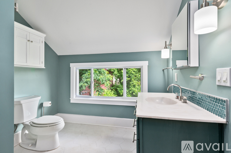 A bathroom with a white toilet, sink, and a window with a view of trees.