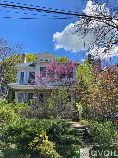 A house with a sign that says "For Sale" is surrounded by greenery and trees.