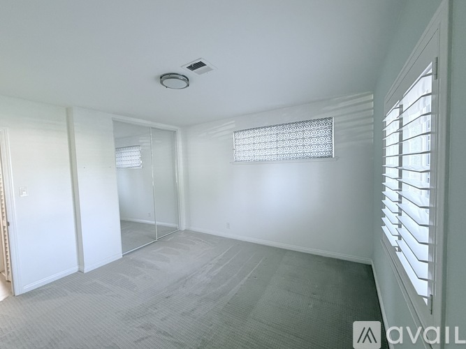 A spacious room with a carpeted floor, a window with blinds, and a ceiling fan.