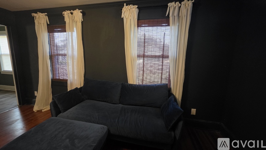 A living room with a black couch and two windows with curtains.