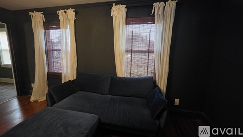 A living room with a black couch and two windows with curtains.