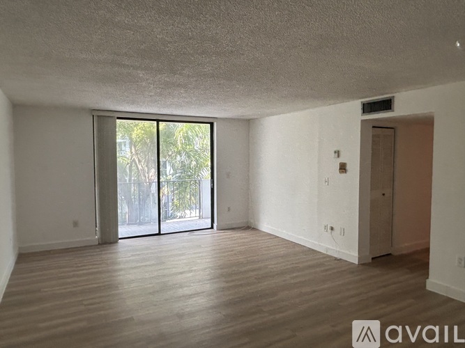 A spacious room with wooden flooring and a sliding glass door leading outside.