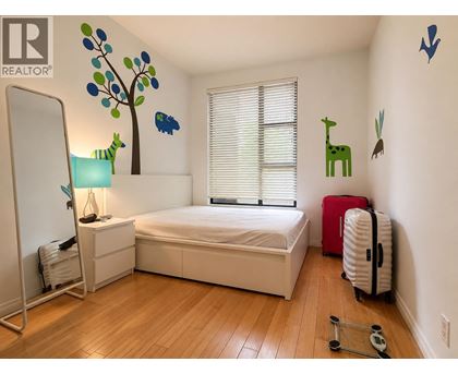 A bedroom with a white bed, a red suitcase, and a wooden floor.