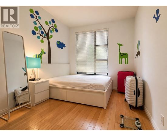A bedroom with a white bed, a red suitcase, and a wooden floor.