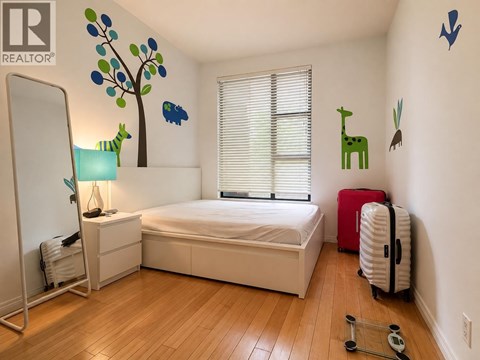 A bedroom with a white bed, a red suitcase, and a wooden floor.