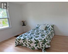 A bedroom with a bed covered in a green leaf print bedspread.