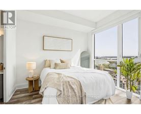 A bedroom with a large bed, a nightstand with a lamp, and a view of the city through the window.