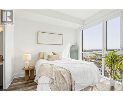 A bedroom with a large bed, a nightstand with a lamp, and a view of the city through the window.