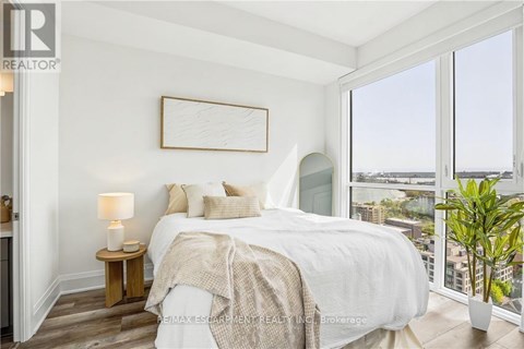 A bedroom with a large bed, a nightstand with a lamp, and a view of the city through the window.