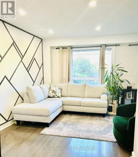 A white couch with a green chair and a rug in front of a window.