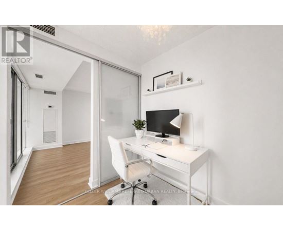 A white desk with a computer and lamp in a room with a white chair and a white wall.