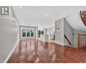 A spacious room with wood flooring and a staircase on the right side.