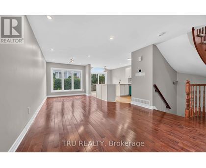 A spacious room with wood flooring and a staircase on the right side.