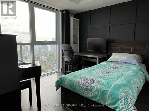 A bedroom with a bed, desk, and chair with a view of the city.