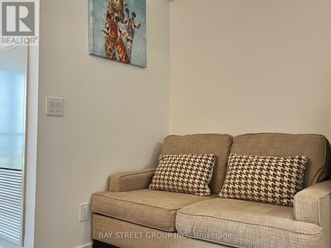 A tan couch with two pillows sits in a room with a giraffe painting on the wall.