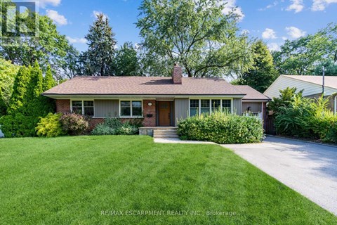 A house with a brown roof and a brick chimney is surrounded by greenery.
