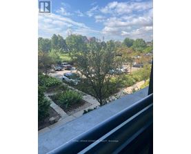 A view from a balcony looking out over a residential area with trees and cars.