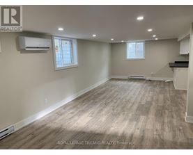 A spacious room with wooden flooring and two windows.
