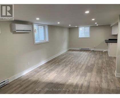 A spacious room with wooden flooring and two windows.