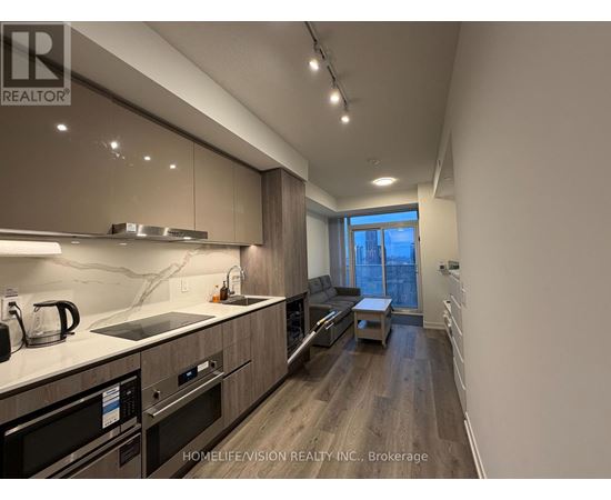 A modern kitchen with dark wood floors and stainless steel appliances.