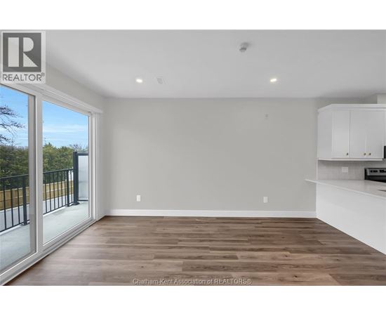 A spacious room with wooden flooring and white walls, part of a real estate listing.
