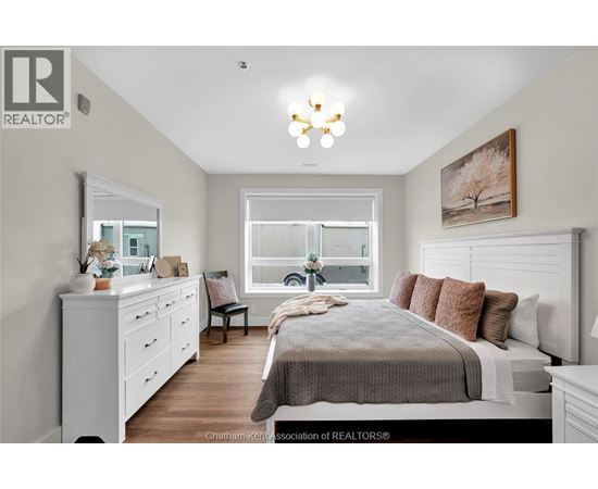 A well-lit bedroom with a large bed, a dresser, and a window.
