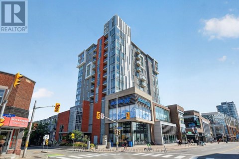 A modern multi-story building with glass windows and a sign that reads "REALTOR" is situated at an intersection with traffic lights and pedestrian crossings.