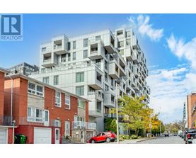 A modern apartment building is situated on a street with cars parked on the side.
