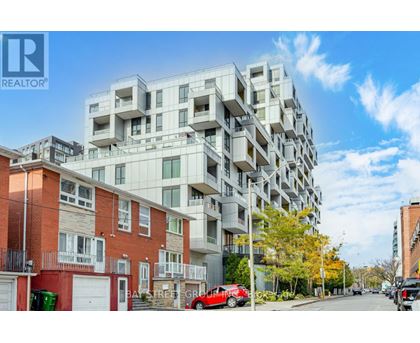 A modern apartment building is situated on a street with cars parked on the side.