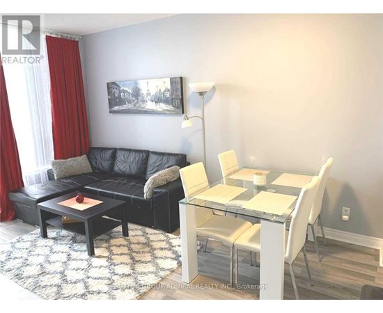 A living room with a black couch, a glass table, and a painting on the wall.