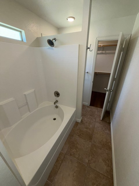 A white bathtub with a shower head and a door to a closet.