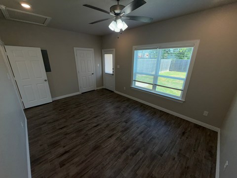 A room with a ceiling fan and a window overlooking a fence.