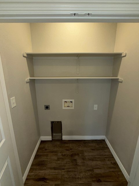 A room with a wooden floor and a white wall with a shelf above it.