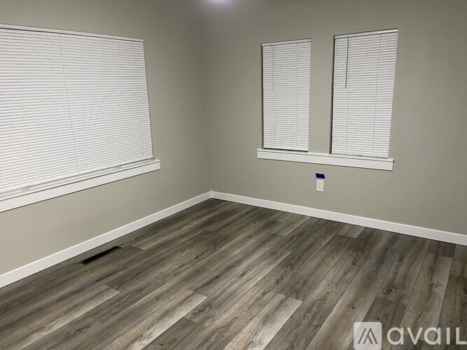 A room with wooden flooring and two windows with blinds.