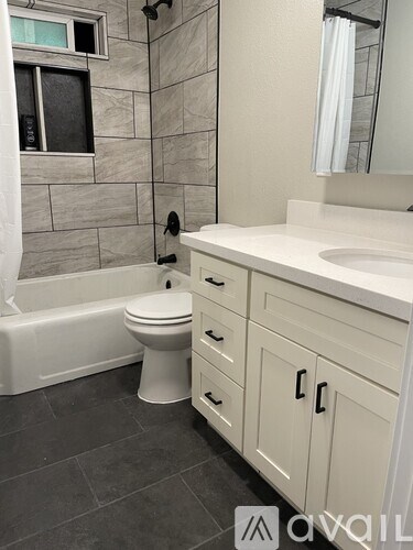 A white toilet sits in a bathroom with a white tub and a sink.