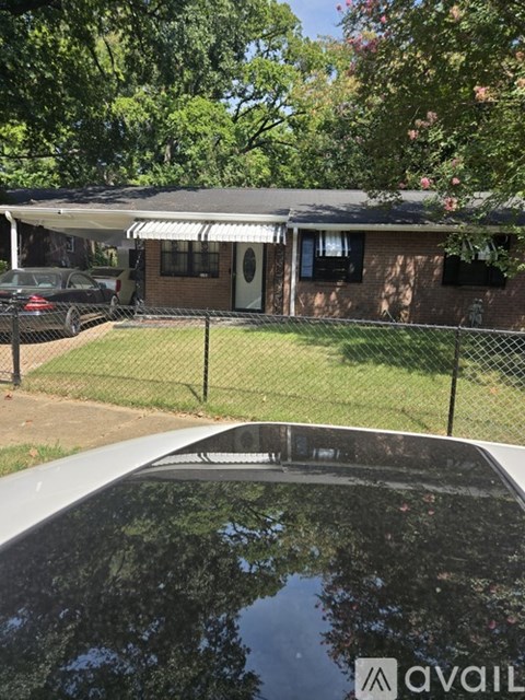 A black car is parked in front of a house with a fence.