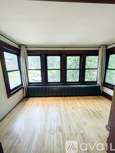 A room with wooden floors and a large window with a view of trees.