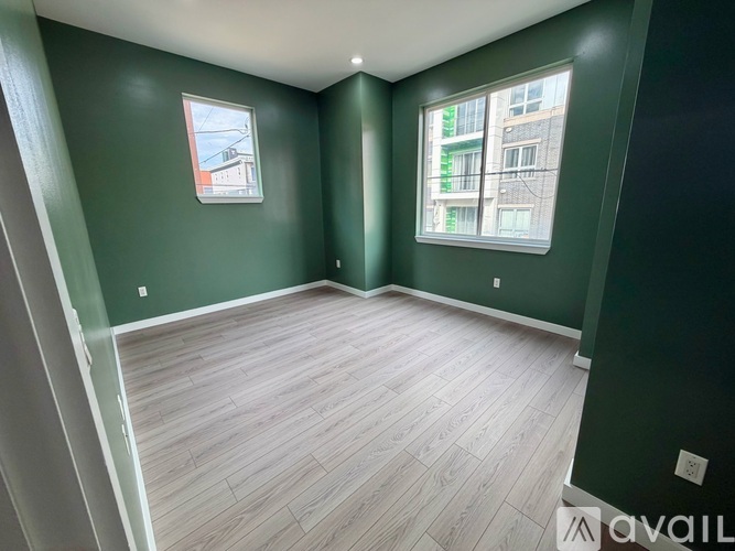 A room with green walls and wood flooring, with a window showing a building outside.