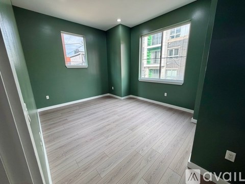 A room with green walls and wood flooring, with a window showing a building outside.