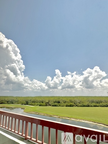 A bridge with a red railing and a logo that reads "ayali" in the foreground with a body of water and greenery in the background.