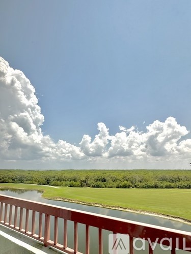 A bridge with a red railing and a logo that reads "ayali" in the foreground with a body of water and greenery in the background.