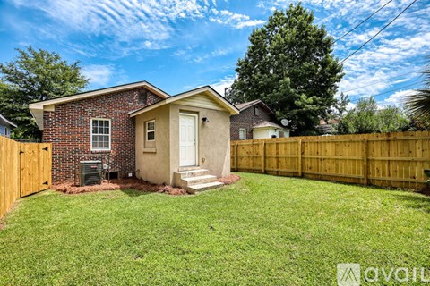 A small house with a brown brick exterior and a white door is surrounded by a wooden fence and green grass.