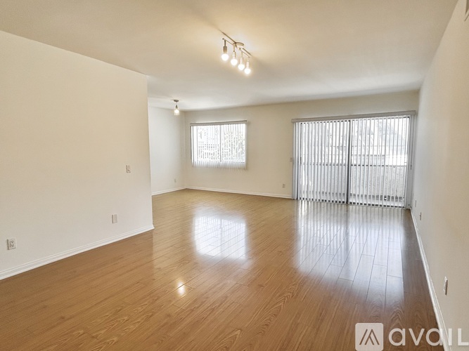 A spacious room with wooden flooring and two windows.
