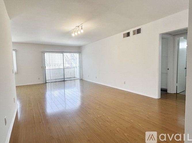 A spacious room with wooden flooring and a large window with blinds.