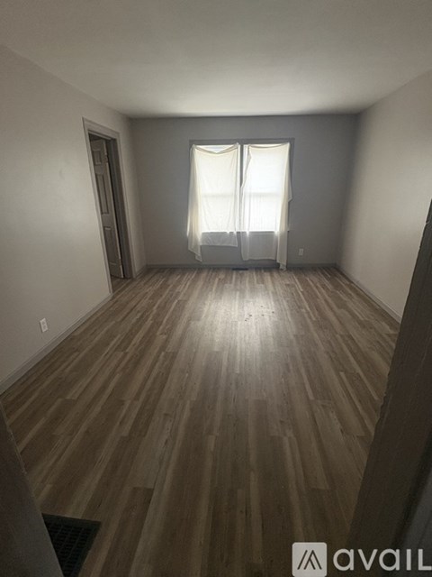 A room with wooden flooring and a window with curtains.