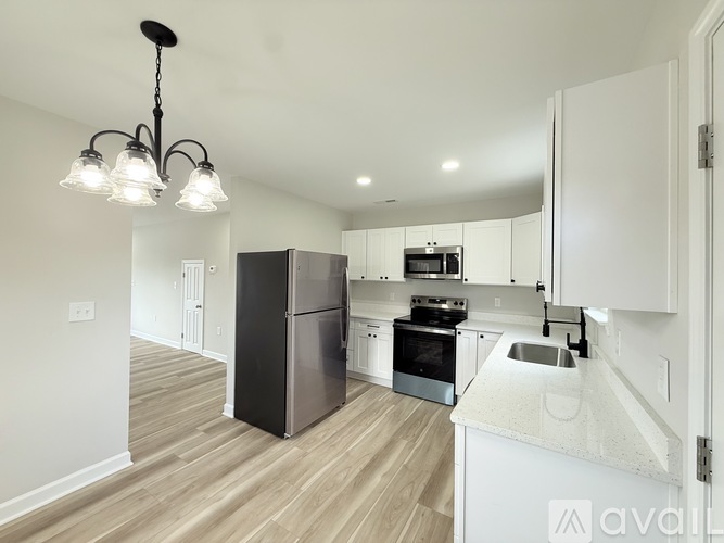 A kitchen with a black refrigerator and stove, white cabinets, and a light wood floor.