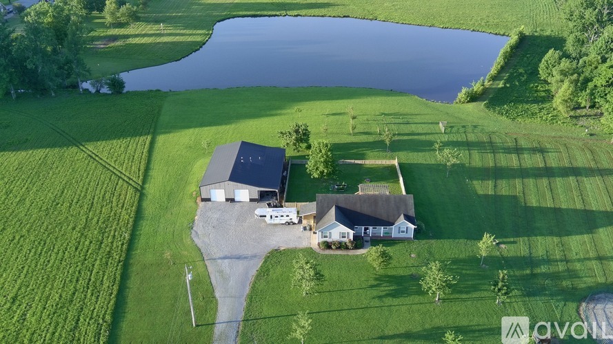 A house with a garage is situated on a grassy field next to a body of water.